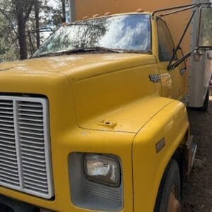 IMG_6626 - Montana Auctions by Kevin Hill Front-left view of a yellow, rusted semi-truck with a large chrome grille and square headlight, parked outdoors.