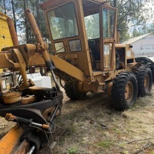 IMG_6628 - Montana Auctions by Kevin Hill Orange wheel loader with a large front attachment sits on a dirt lot among trees, weathered and awaiting maintenance, with an open cabin door visible.