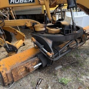 IMG_6629 - Montana Auctions by Kevin Hill Close-up of a yellow HUBER heavy construction machine with hydraulic arms and a rusted attachment on a dirt/gravel surface.