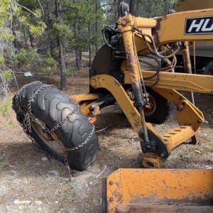 IMG_6630 - Montana Auctions by Kevin Hill Orange construction excavator parts with a chained tire in a pine forest clearing