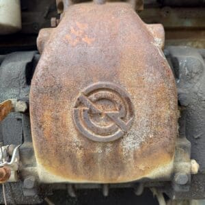 IMG_6632 - Montana Auctions by Kevin Hill Close-up of a rusted industrial engine component with a circular embossed logo and orange chalk markings on a weathered metal surface.