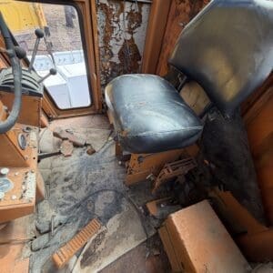IMG_6637 - Montana Auctions by Kevin Hill Interior of an old orange bus with a torn seat, peeling walls, and a dusty, debris-strewn floor with exposed pedals and controls.