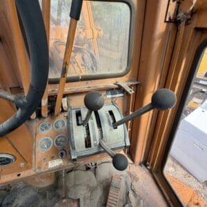 IMG_6639 - Montana Auctions by Kevin Hill Inside a dusty orange construction vehicle cab with multiple black gear levers and worn pedals visible on a dirty floor.