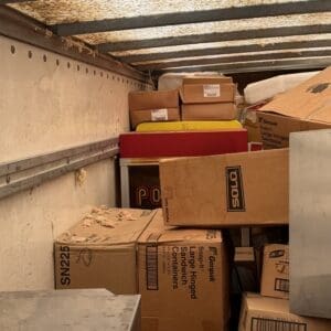 IMG_6644 - Montana Auctions by Kevin Hill Interior of a moving truck with stacked cardboard boxes and packaging materials along the walls, dimly lit ceiling above