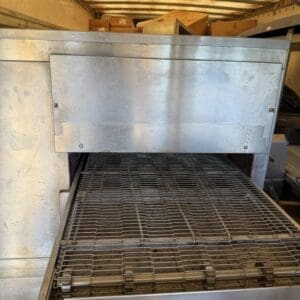 IMG_6646 - Montana Auctions by Kevin Hill Industrial stainless steel conveyor oven/grill inside a truck trailer, with an empty wire-mesh belt and cardboard boxes visible in the rear bay