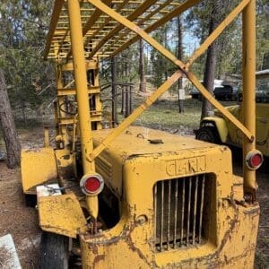 IMG_6649 - Montana Auctions by Kevin Hill Yellow industrial boom crane on a rugged forest site, rusted and weathered with a lattice framework overhead.