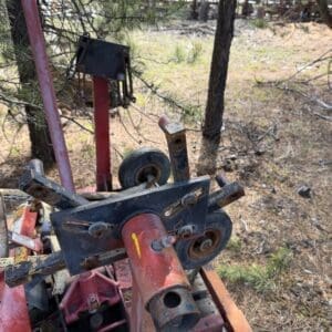 IMG_6656 - Montana Auctions by Kevin Hill Rusty, abandoned farming equipment with red and orange metal frames and wheels in a pine yard.