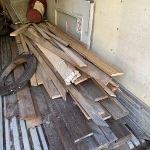 IMG_6657 - Montana Auctions by Kevin Hill Pile of weathered wooden boards and scraps stacked in a dusty storage space or trailer interior with a red industrial fan nearby.