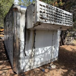 IMG_6660 - Montana Auctions by Kevin Hill Worn, rusted refrigerated trailer with Thermo King cooling unit on top, outdoors among trees and debris.