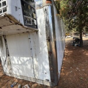 IMG_6661 - Montana Auctions by Kevin Hill Weathered aluminum trailer lying on its side in a park, with a control panel and rusted latches.