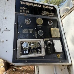 IMG_6662 - Montana Auctions by Kevin Hill Close-up of a weathered Thermo King trailer control panel with gauges, switches, and labeled dials on a dirty black plate, outdoors by a white trailer.