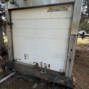 IMG_6664 - Montana Auctions by Kevin Hill Large white industrial equipment trailer with a roll-up door, labeled Fallsway Equipment Company, outdoors on dirt with pine needles and a car in the background.