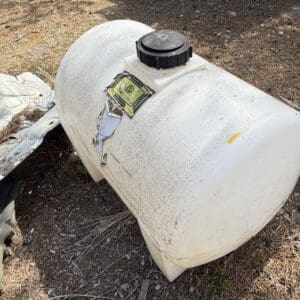 IMG_6665 - Montana Auctions by Kevin Hill White plastic portable fuel tank lying on dirt/grass with a black screw cap and peeling labels.