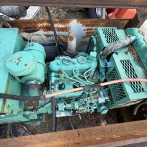 IMG_6667 - Montana Auctions by Kevin Hill Teal industrial engine in a rusted metal frame, with hoses and wires around it outdoors.