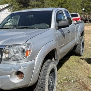 IMG_6671 - Montana Auctions by Kevin Hill Silver pickup truck parked on a dirt lot with trees in the background, front left wheel turned and visible wheel tread.