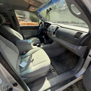 IMG_6674 - Montana Auctions by Kevin Hill Interior of a gray car showing front seats, steering wheel, and center console with gear shifter, daytime sunlight through the windshield and open driver door.