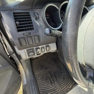 IMG_6679 - Montana Auctions by Kevin Hill Driver's-side dashboard and steering wheel with air vent, switches, and a textured rubber floor mat visible from the driver's seat.