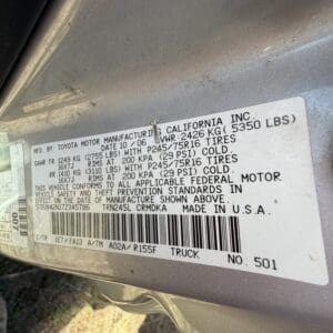 IMG_6681 - Montana Auctions by Kevin Hill Vehicle data sticker on a gray door jamb showing manufacturing details, weights, tire sizes, and barcode (Toyota truck).