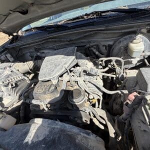 IMG_6682 - Montana Auctions by Kevin Hill Open hood of a dusty vehicle showing the engine bay with hoses, belts, and the air filter housing visible.