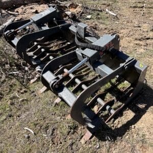 IMG_6684 - Montana Auctions by Kevin Hill Skid-steer grapple attachment with curved jaws and multiple tines on dirt ground, ready for debris handling.