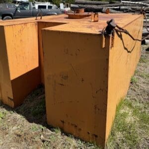 IMG_6688 - Montana Auctions by Kevin Hill Two large orange rusted metal containers outdoors, with a rope hooked on top; truck and logs in the background.