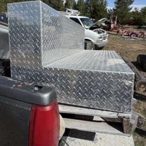 IMG_6692 - Montana Auctions by Kevin Hill Diamond-plate aluminum storage box on a trailer in a yard, with a pickup truck nearby and its hood open in the background.