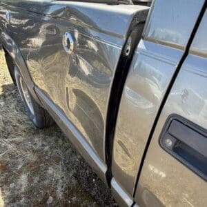 IMG_6695 - Montana Auctions by Kevin Hill Close-up of a gray pickup truck showing a dented side panel and an open bed loaded with rusted metal pieces.
