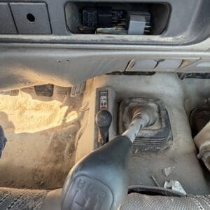 IMG_6699 - Montana Auctions by Kevin Hill Manual transmission gear shifter in the foreground inside a dusty vehicle, with exposed wiring and dash area above.