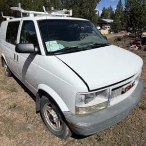 IMG_6704 - Montana Auctions by Kevin Hill White GMC cargo van with a roof rack on a dirt lot; hood slightly ajar and front bumper scuffed.