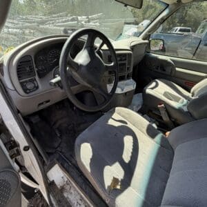 IMG_6706 - Montana Auctions by Kevin Hill Interior of a dusty pickup truck with a torn driver's seat and dirty floor mats, parked near logs in a forested area outside the cab
