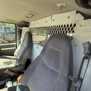 IMG_6708 - Montana Auctions by Kevin Hill Interior of a cargo van showing front seats and a diamond-mapped metal partition behind them with dirt marks and scattered debris on the floor.