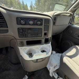 IMG_6709 - Montana Auctions by Kevin Hill Interior of a vehicle with a dirty center console and litter on the floor, including used tissues and cups nearby.