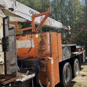IMG_6717 - Montana Auctions by Kevin Hill Orange crane truck with a long white boom, parked on grassy ground with trees in the background.