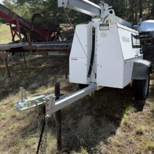 IMG_6728 - Montana Auctions by Kevin Hill Towable white industrial machine on a trailer with a long hydraulic boom, parked in a grassy, wooded lot.