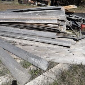 IMG_6744 - Montana Auctions by Kevin Hill Large pile of weathered gray wooden planks stacked haphazardly in an outdoor storage yard.