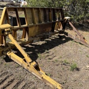 IMG_6748 - Montana Auctions by Kevin Hill Old, rusty yellow farming implement lying in a dirt field with trees in the background; appears to be a discontinued attachment (possibly a seed drill or similar equipment).