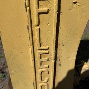 IMG_6749 - Montana Auctions by Kevin Hill Close-up of a yellow metal post with a vertical raised logo/word that appears to read 'FELLIC', showing worn paint and dirt.