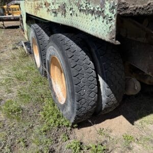 IMG_6756 - Montana Auctions by Kevin Hill Rusty green flatbed trailer with dual wheels and orange rims, weathered paint, parked on dirt with weeds nearby.