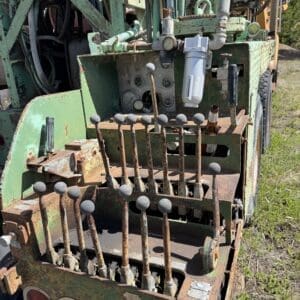 IMG_6757 - Montana Auctions by Kevin Hill Old, rusty agricultural machine with a row of metal levers and gray knobs at the back, faded green paint and exposed hydraulics.