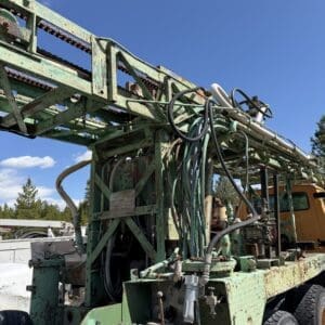 IMG_6758 - Montana Auctions by Kevin Hill Rusty green industrial machinery with cables and levers mounted on a wheeled platform, exposed under bright blue sky.