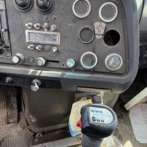 IMG_6761 - Montana Auctions by Kevin Hill Dusty dashboard of an old truck with round gauges, a vintage radio, and a prominent gear shift lever in the foreground, all showing wear and dirt.