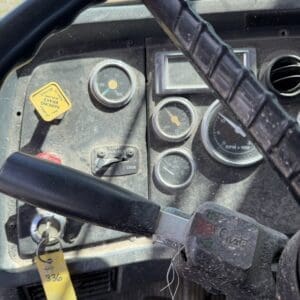 IMG_6762 - Montana Auctions by Kevin Hill Close-up of a dusty truck dashboard: steering wheel, several analog gauges, ignition with key, and a yellow labeled control knob on the left.
