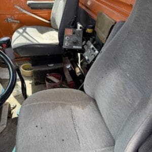 IMG_6763 - Montana Auctions by Kevin Hill Interior of an old orange truck cab with worn gray seats and exposed controls between the seats.