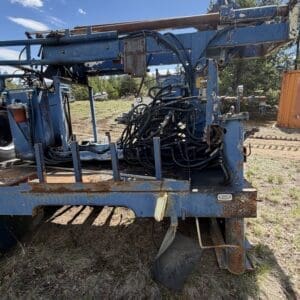 IMG_6769 - Montana Auctions by Kevin Hill Old, rusted blue hydraulic farming implement on a trailer with tangled hoses in a grassy lot under a blue sky.
