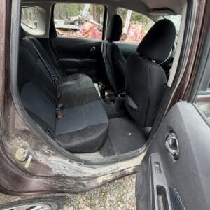 IMG_6775 - Montana Auctions by Kevin Hill Back seat area of a dusty brown car with black fabric seats and clutter on the floor; rear door is open and rocky ground is visible outside.