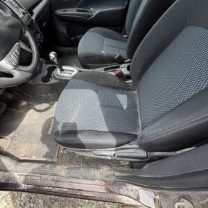 IMG_6779 - Montana Auctions by Kevin Hill Interior of a dusty car with front seats, gear shifter, and steering wheel; driver's door open showing rocky ground outside.