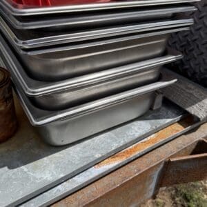 IMG_6786 - Montana Auctions by Kevin Hill Stack of metal baking pans nested inside a red crate on a rusted workshop table.