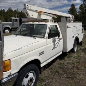 IMG_6787 - Montana Auctions by Kevin Hill White Ford F-250 utility truck with a large bucket lift mounted on the service body, parked in a grassy lot with trees in the background.