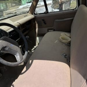IMG_6791 - Montana Auctions by Kevin Hill Dusty brown pickup truck interior with a worn bench seat, steering wheel, and dirt on the dashboard; debris visible through the windows.