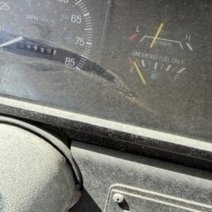 IMG_6793 - Montana Auctions by Kevin Hill Dusty truck dashboard showing speedometer up to 85 mph, fuel gauge near E, and a label reading 'Unleaded Fuel Only' with a key ignition panel nearby.